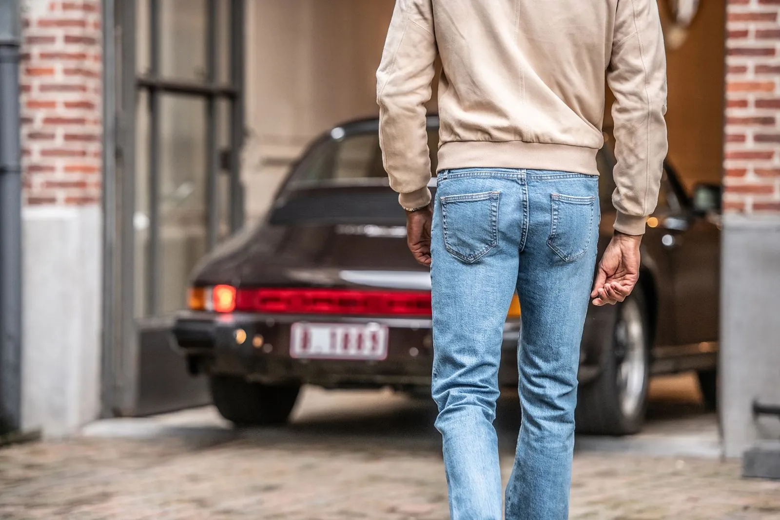 Férfi világos farmerben egy klasszikus autó felé sétál